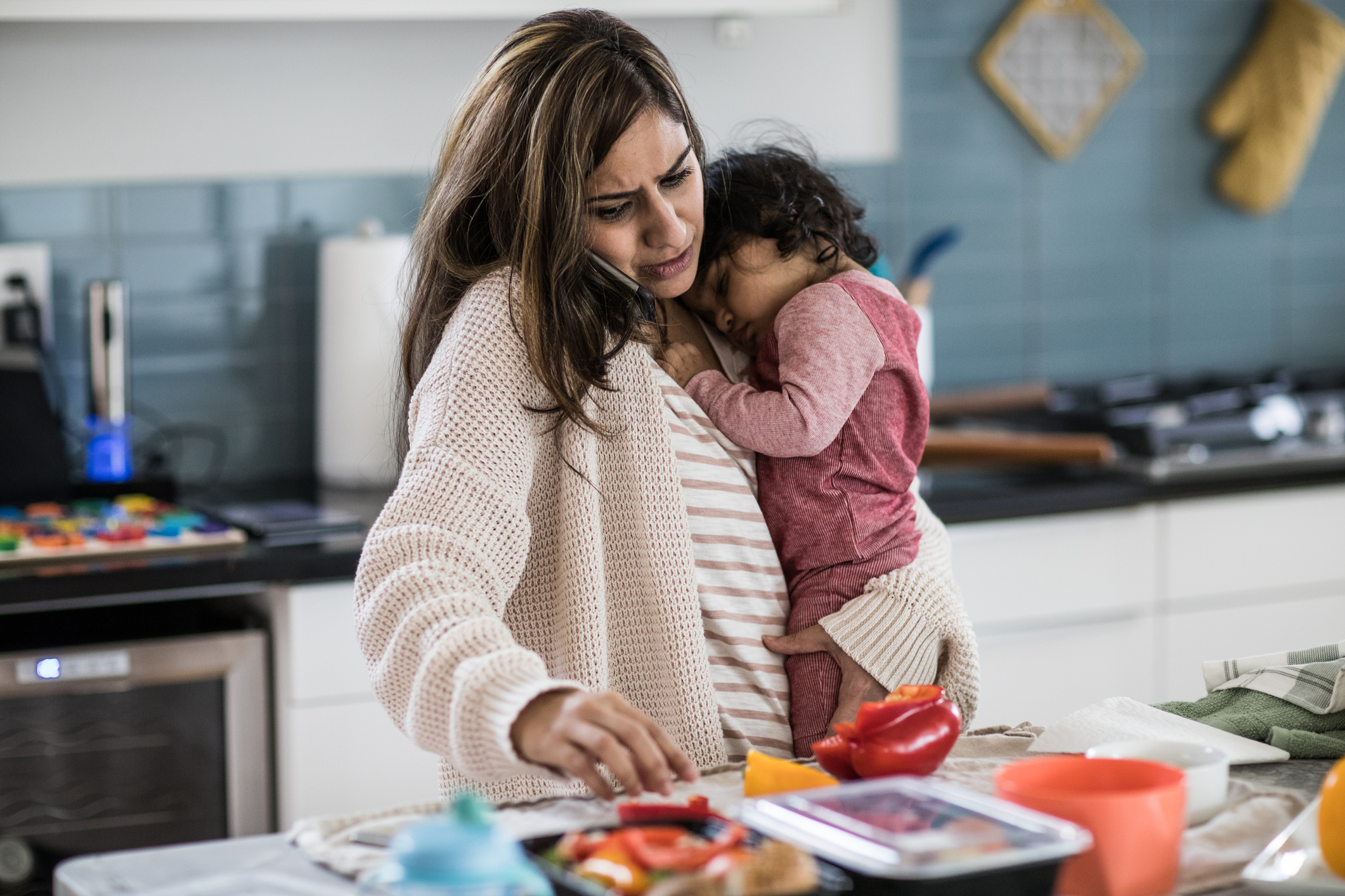 Woman preparing food while holding a toddler in a kitchen