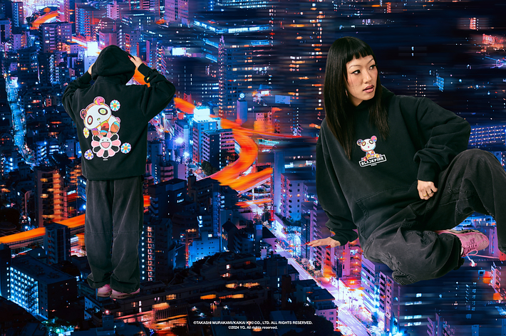 Woman in oversized hoodie with graphic design sits against a backdrop of city lights. Style exudes urban cool vibe