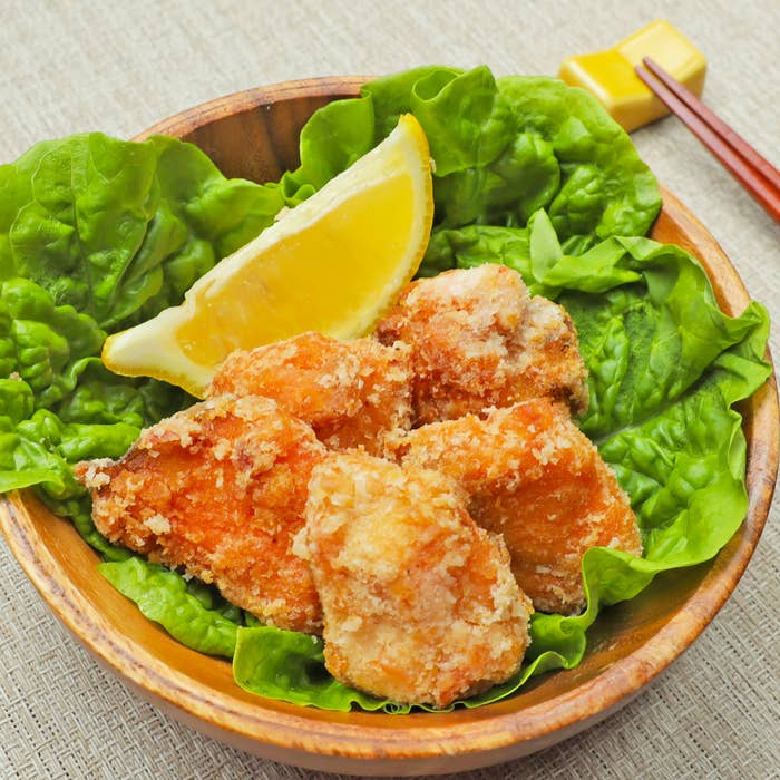 レタスが敷かれた木製のボウルにレモンと共に盛り付けられたフライドチキン。