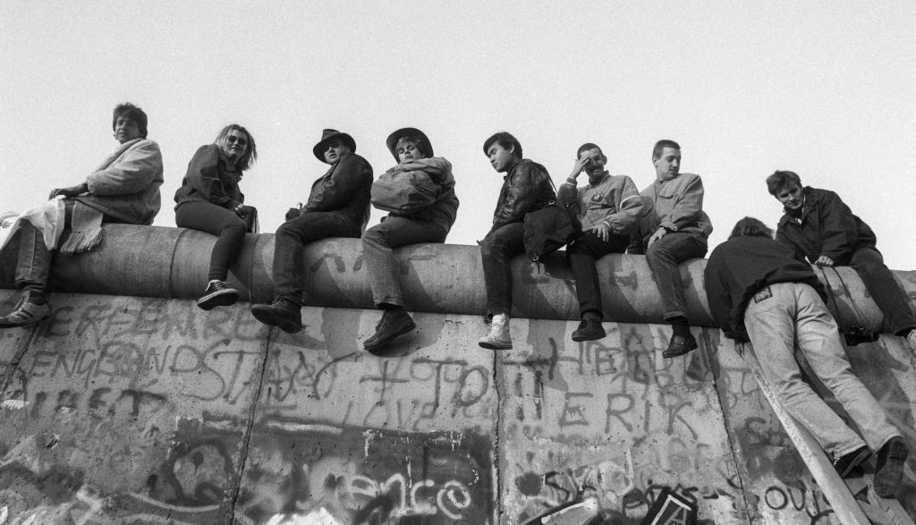 People sitting atop a graffiti-covered wall, appearing casual and relaxed