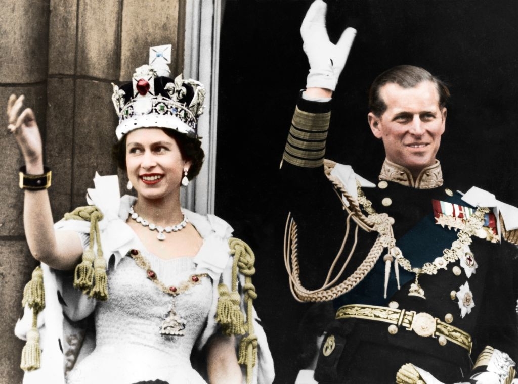 Queen Elizabeth II and Prince Philip waving from a balcony, dressed in formal regalia