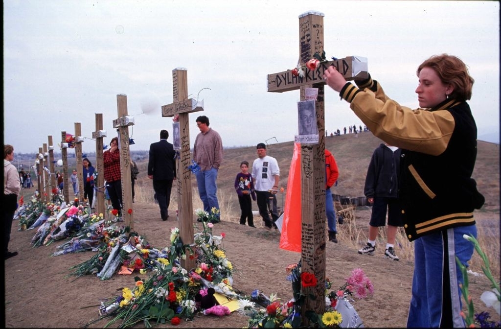 A memorial with crosses and flowers; individuals paying respects