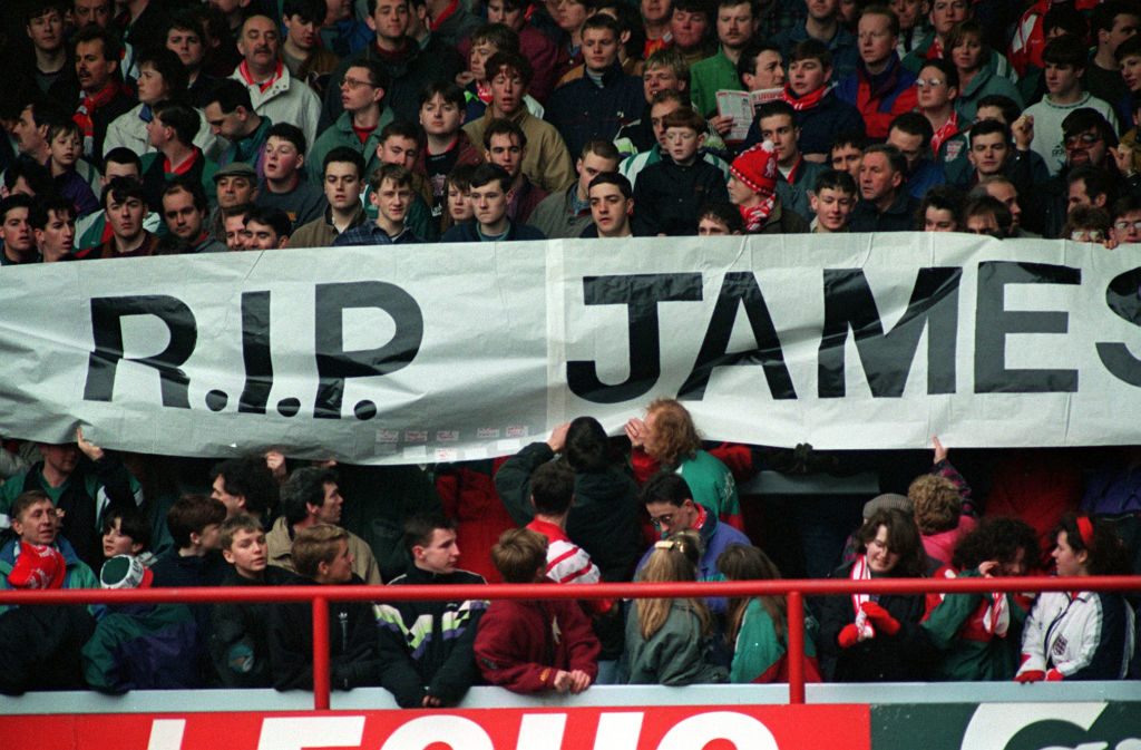 A crowd of fans at a sporting event holding up a banner with the text &quot;R.I.P. JAMES.&quot;