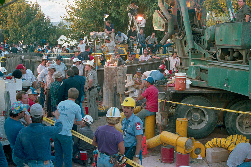 Rescue workers and onlookers gather around a well during a rescue operation