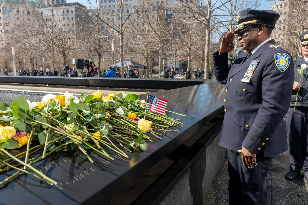 Officer saluting at 9/11 Memorial with floral tributes and U.S. flag
