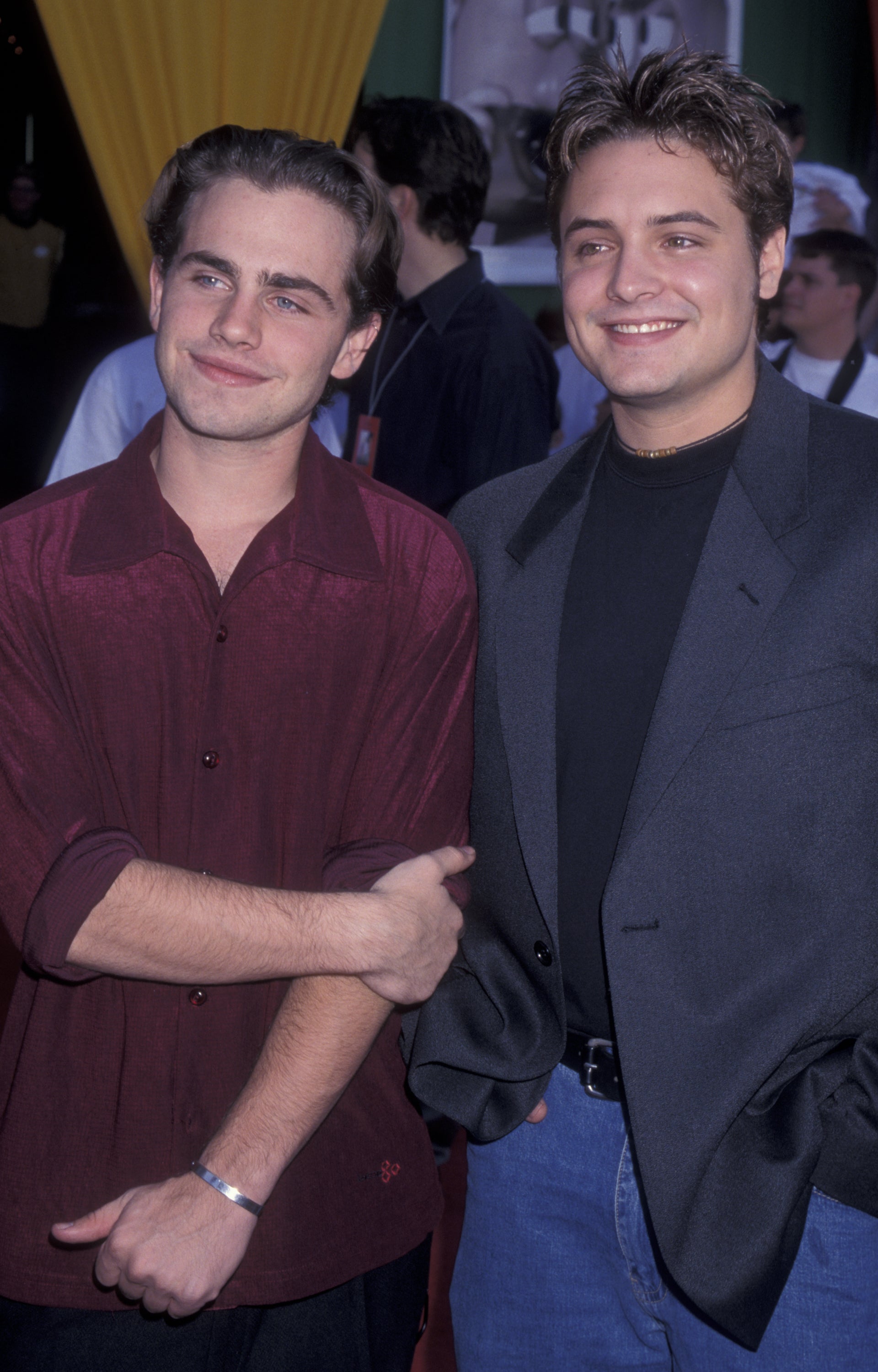 Two men smiling at an event; one in a dark shirt and jacket, the other in a maroon button-up shirt