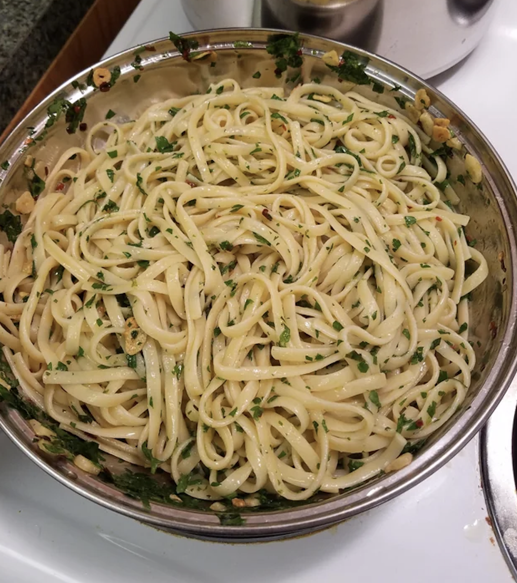 A bowl of linguine pasta with chopped herbs and visible spices