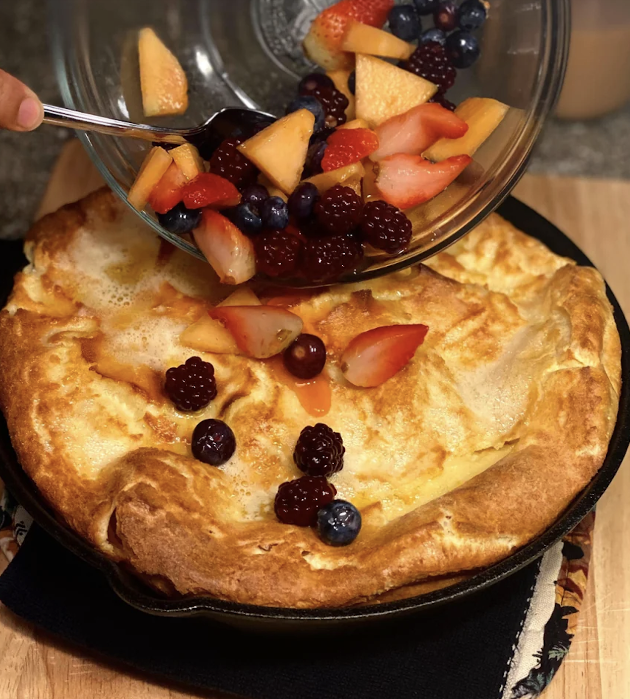 Puffed golden-brown pancake in skillet topped with assorted fresh berries and fruit slices