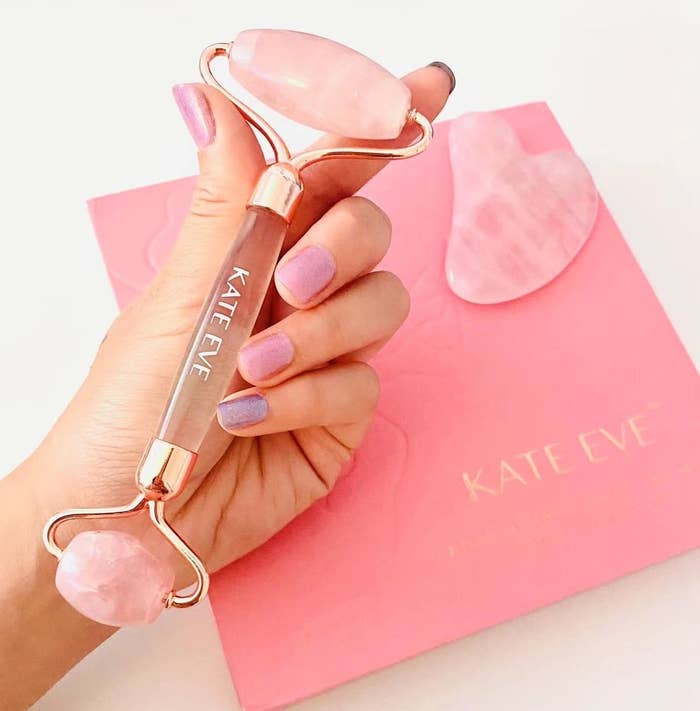 Hand holding a rose quartz facial roller above a pink envelope with &quot;KATE EVE&quot; branding