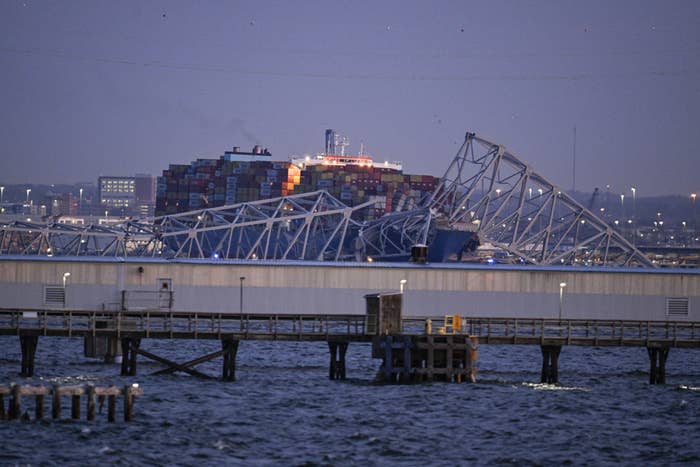Collapsed section of a bridge with a cargo ship in the background at dusk