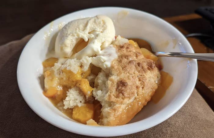 Peach cobbler in a bowl with a scoop of vanilla ice cream, with a spoon
