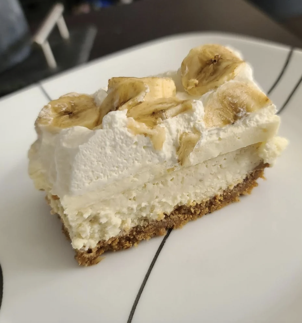 Slice of banana cream pie with fresh banana slices on top, on a white plate