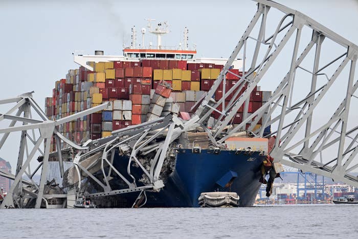 A large cargo ship crashed into a bridge, causing structural damage with containers visible. No people in the image