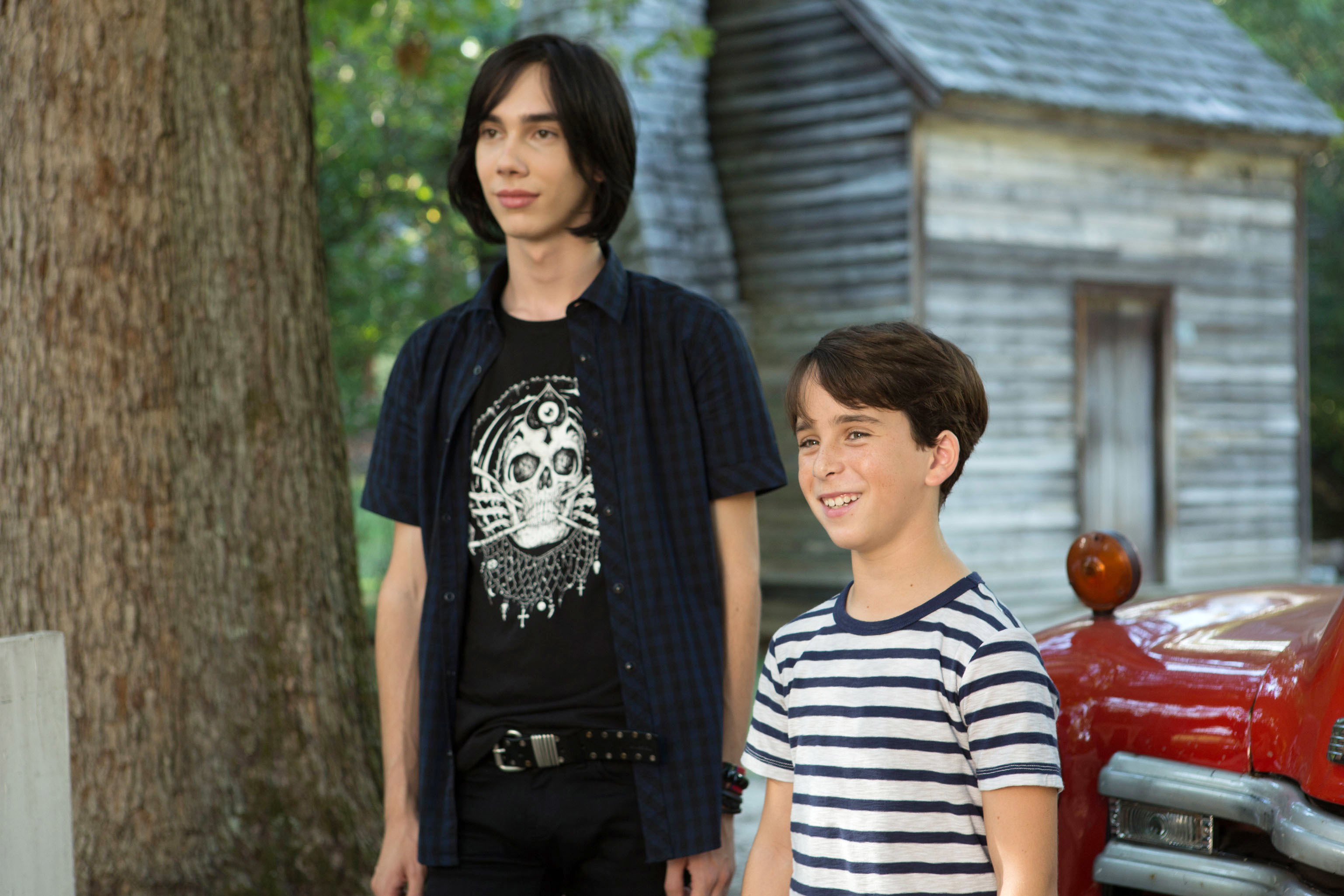 Charlie in a skull graphic T-shirt and Jason Drucker in a striped shirt, standing outside near a cabin in the movie