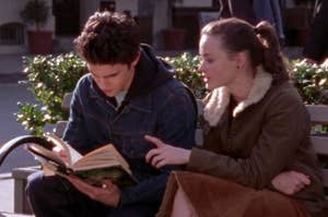Two characters from the show "Glee," a male and a female, sitting on a bench reading a book together