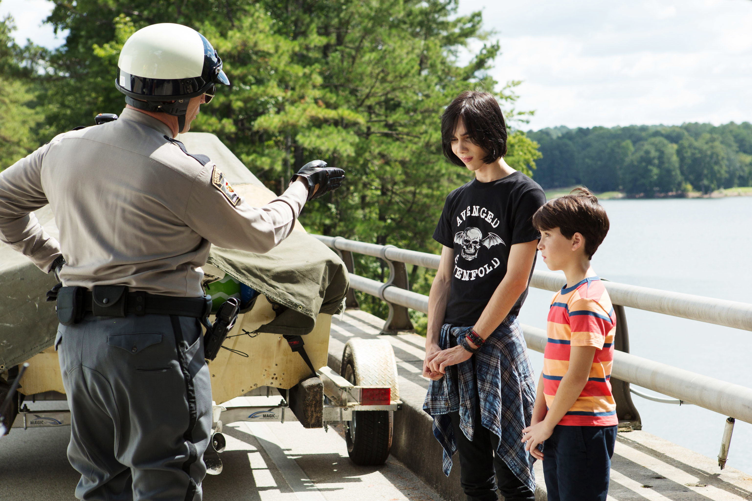 A police officer interacts with two young boys by a lake, one wearing a &quot;Chicago&quot; T-shirt, the other in stripes