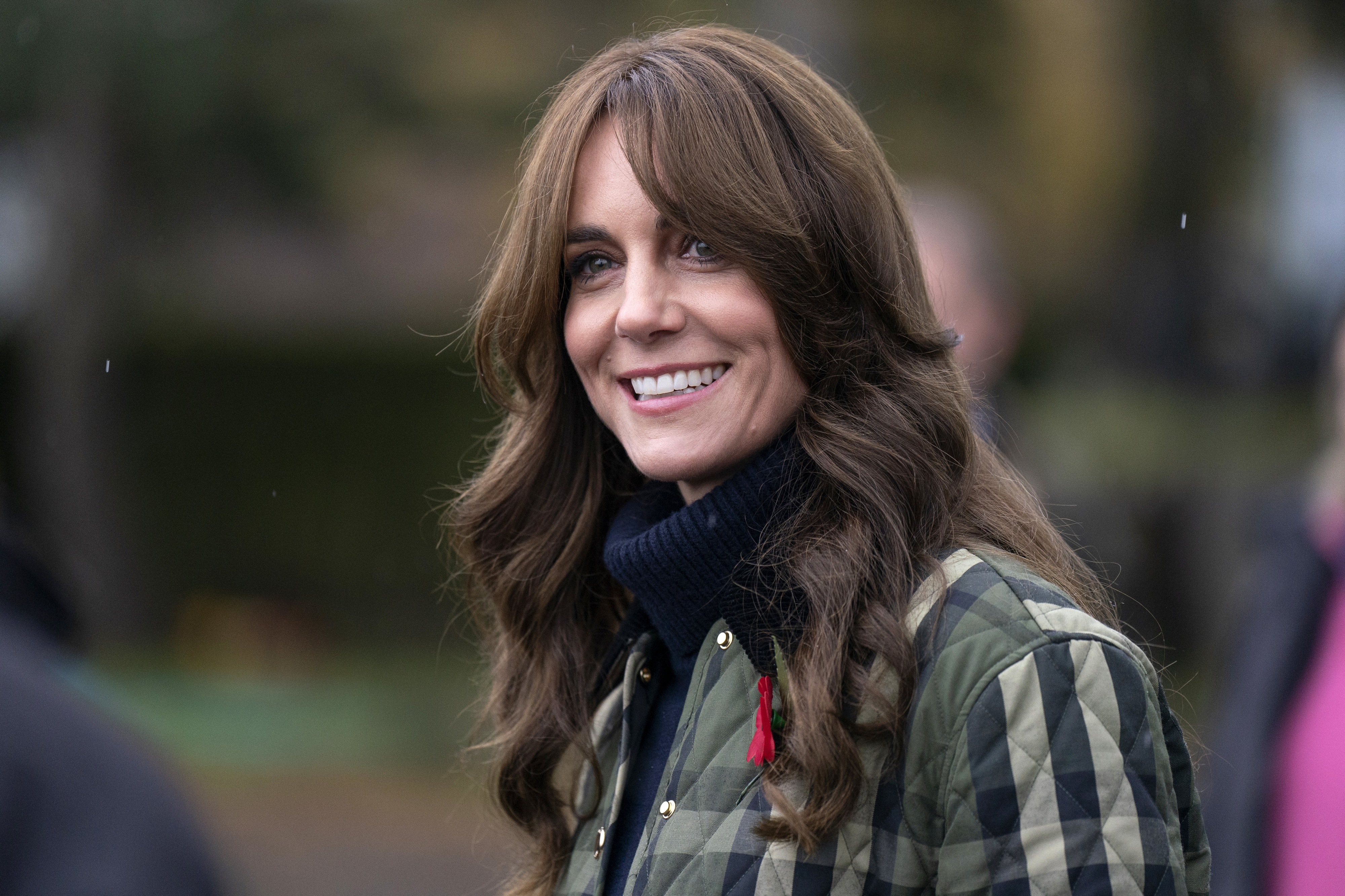 Kate Middleton wearing a quilted jacket, smiles during an outdoor event