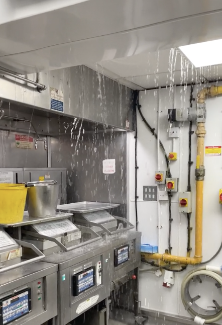 Industrial kitchen with water spraying from a burst pipe above deep fryers
