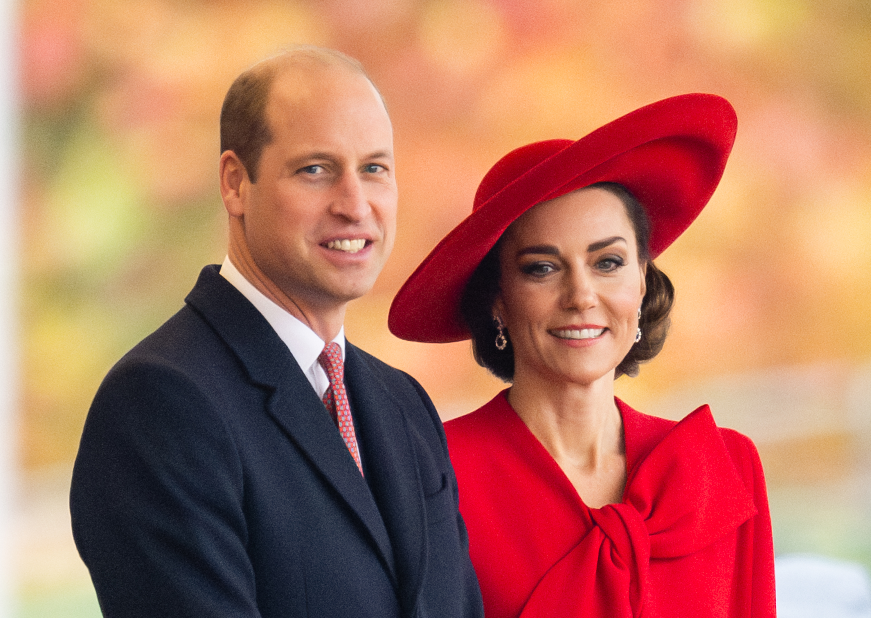 Prince William and Kate Middleton in formal attire, Kate in a red hat and matching outfit