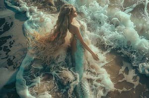Mermaid with long hair sitting on shore, touching the foam of a wave