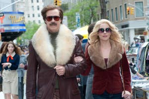 Two characters from the movie "Anchorman 2" walk confidently on a city street, donning 70s outfits with prominent fur collars