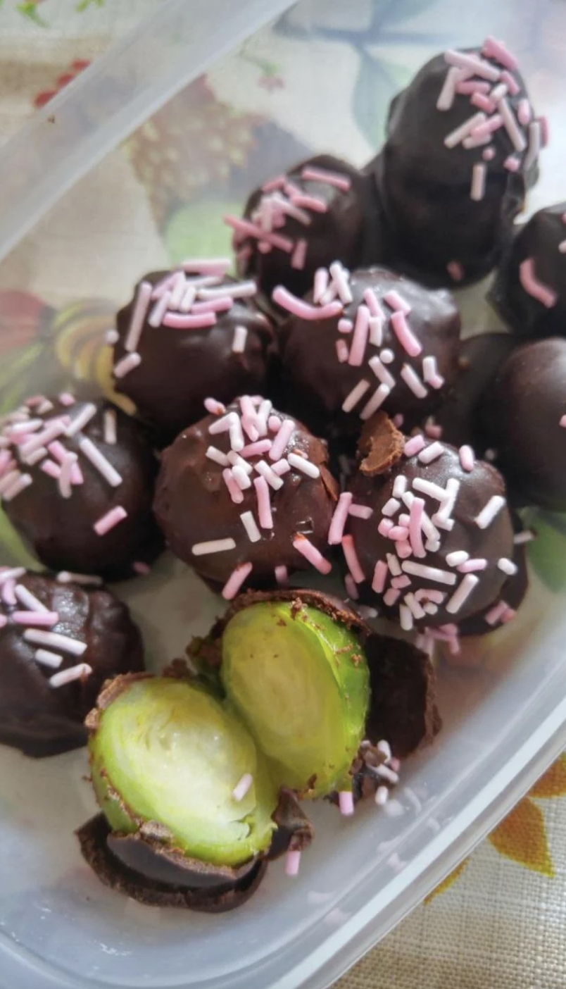 Chocolate-covered treats with sprinkles, some cut in half showing a green interior, in a container