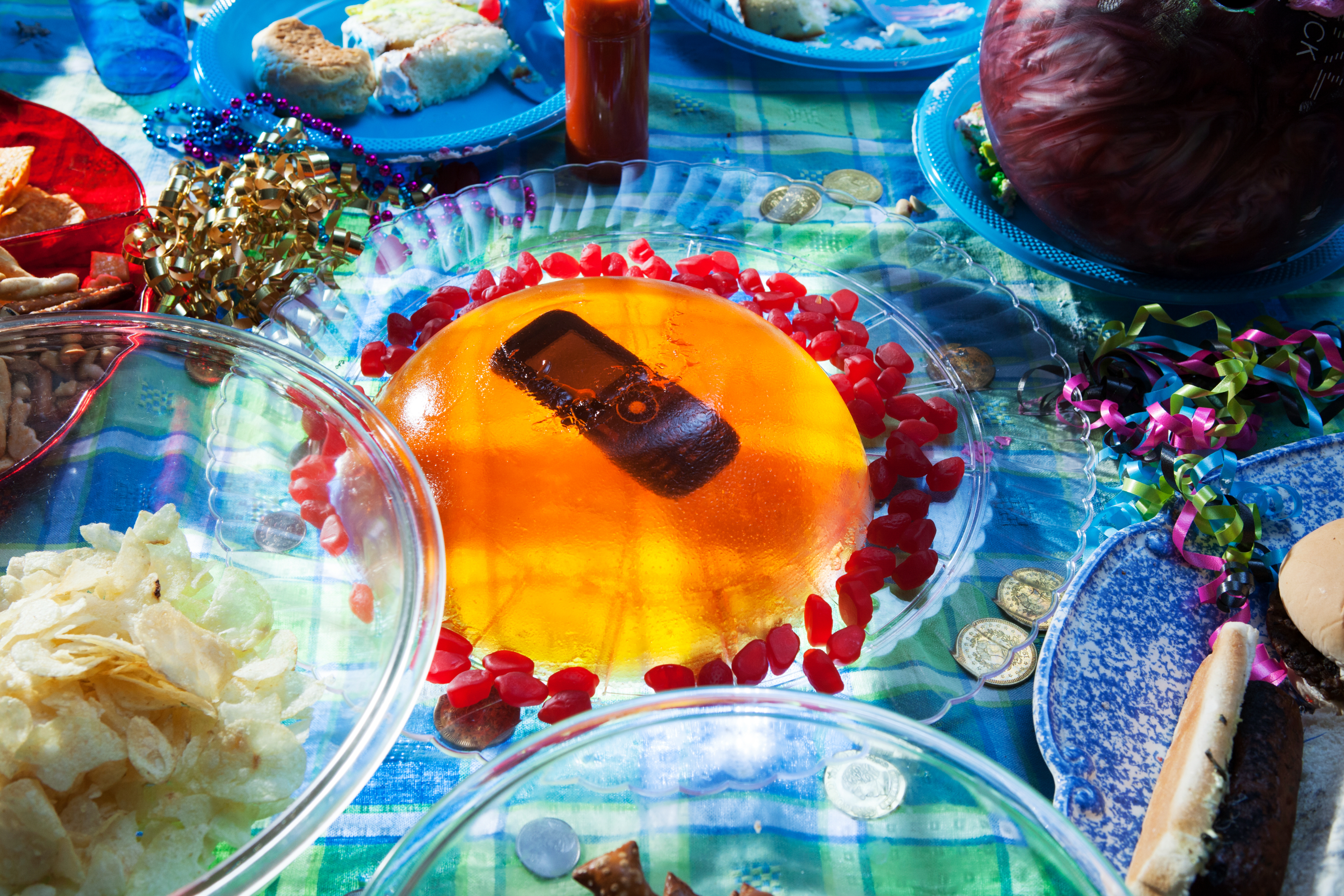 A transparent gelatin dessert with a stapler suspended inside, surrounded by a variety of food items on plates