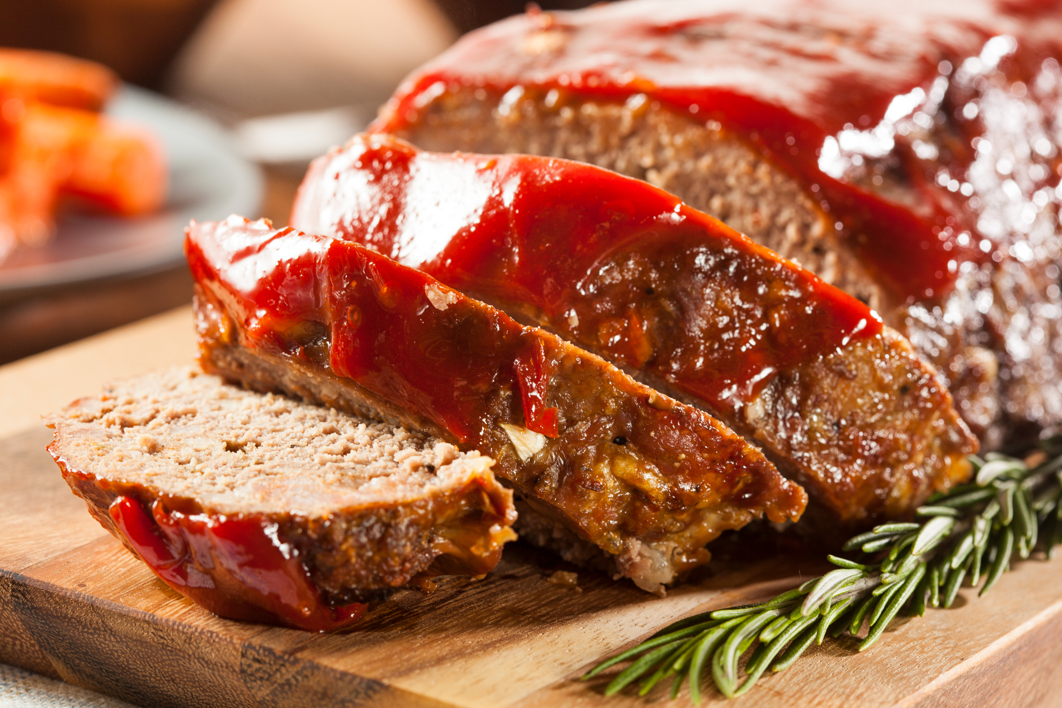 Sliced meatloaf on a wooden board with rosemary sprig, focus on texture
