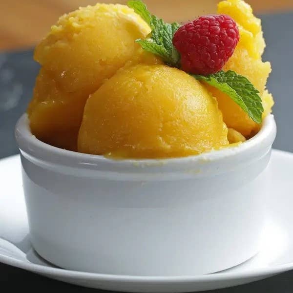 Scoops of mango sorbet in a bowl garnished with a raspberry and mint leaf