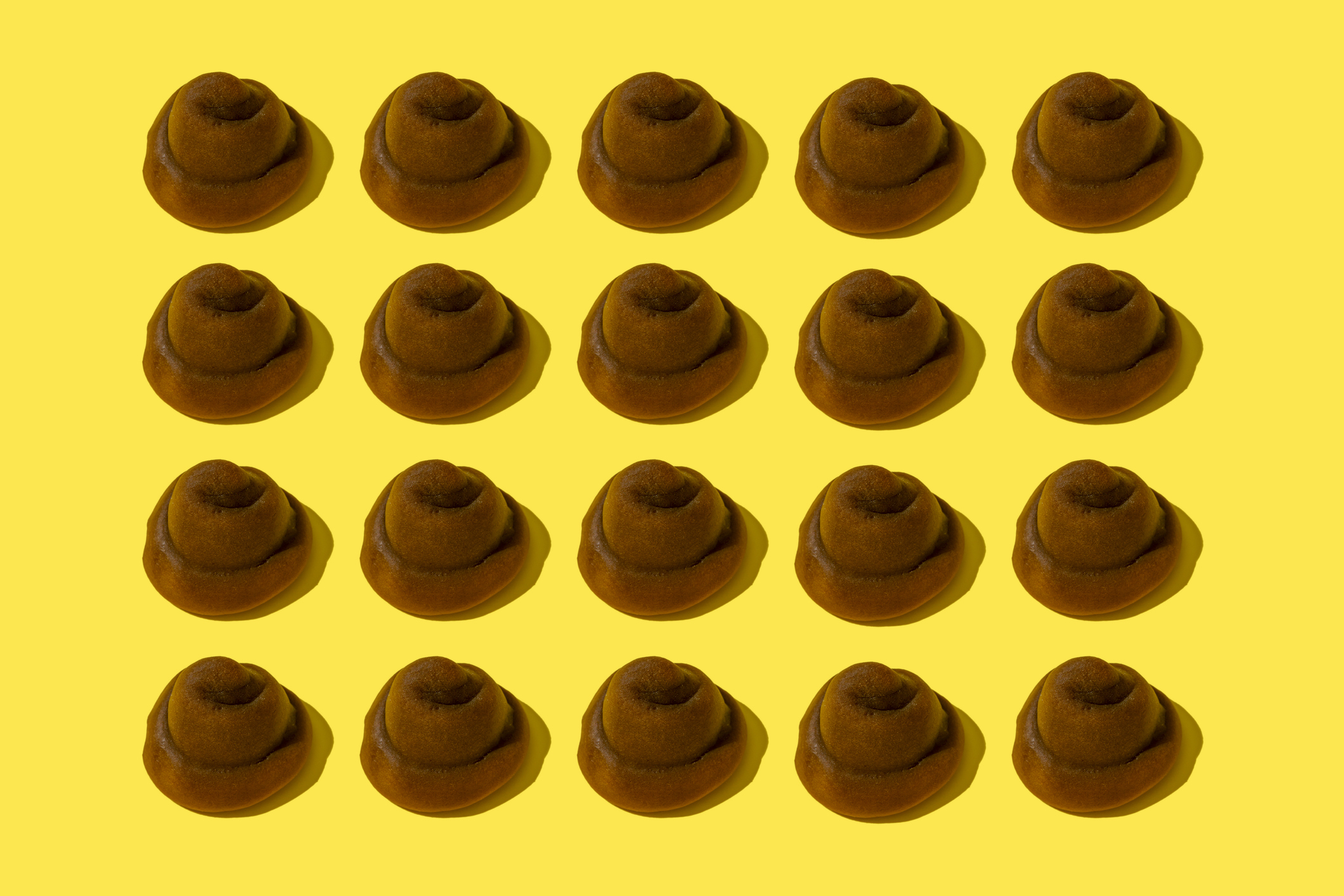 Multiple brown felt hats arranged in a grid pattern on a yellow background
