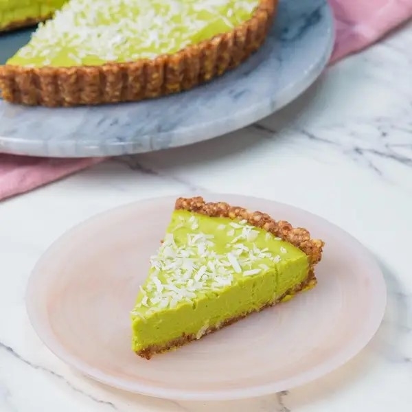 A slice of avocado pie on a plate, with the rest of the pie in the background