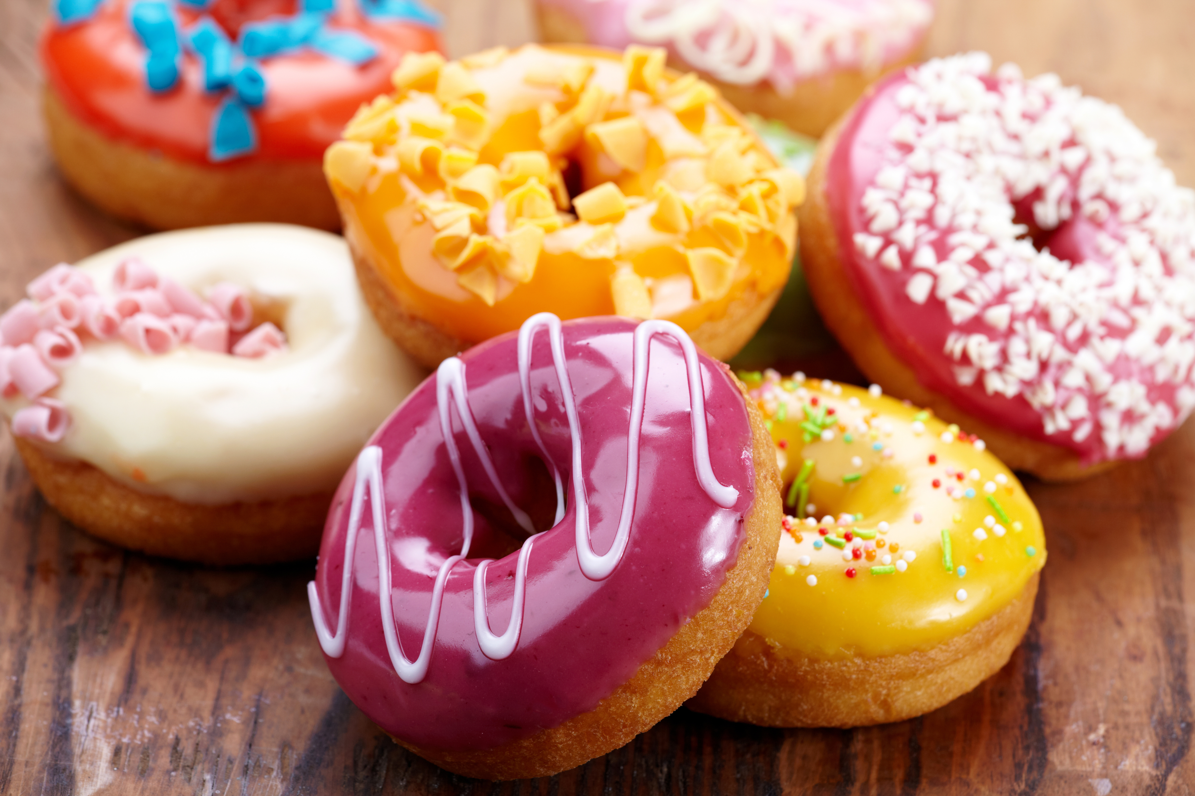 A variety of donuts with different icings and toppings are shown on a wooden surface