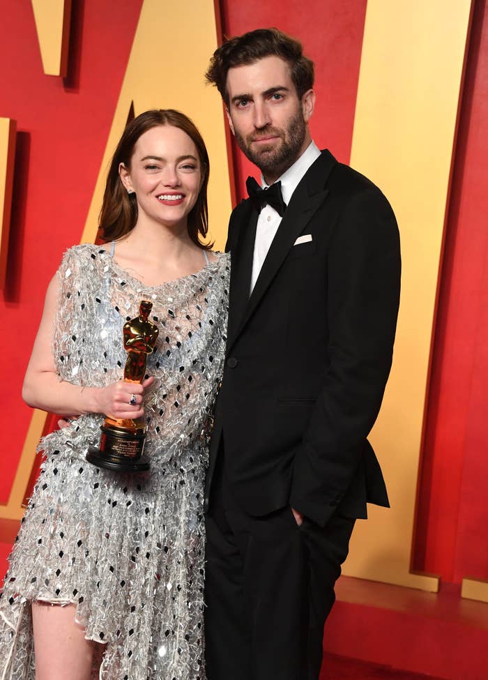 Emma Stone in a beaded dress holds an Oscar, standing next to Dave McCary in a tuxedo