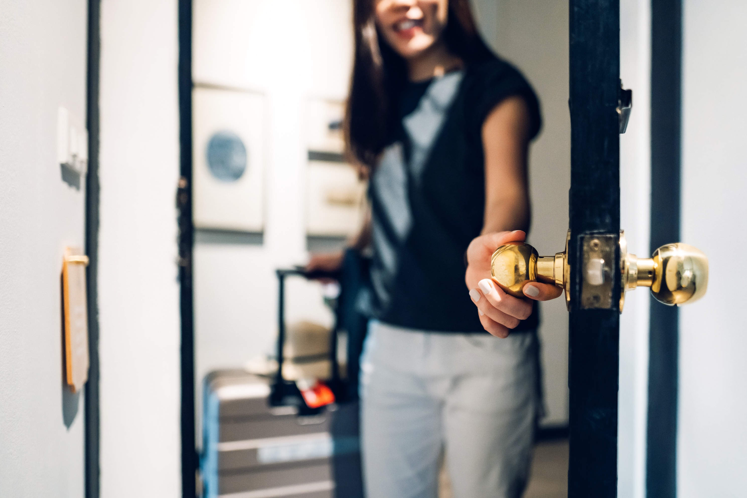 Woman opening a door, smiling, focus on door handle