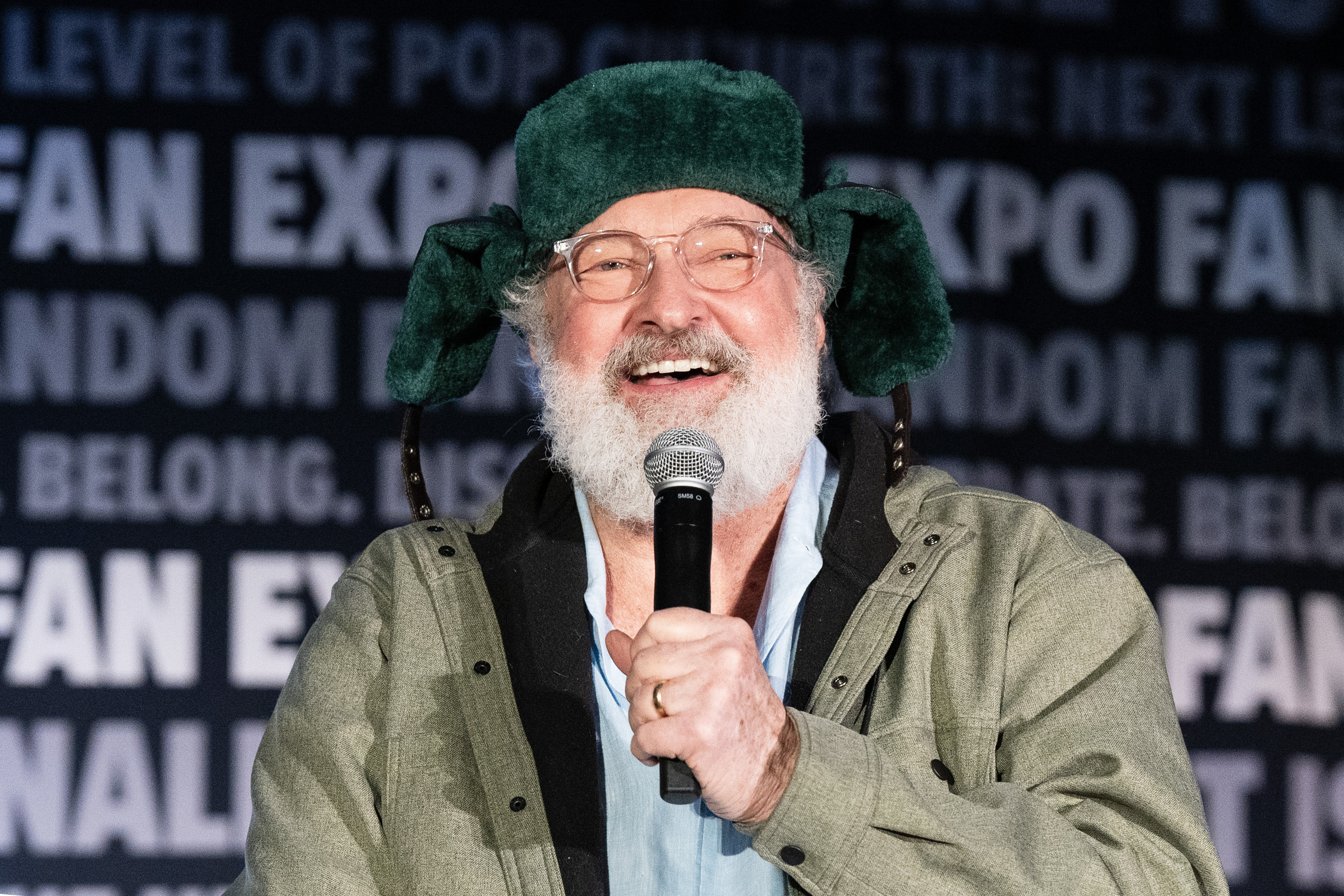Randy onstage speaking into a microphone, wearing a whimsical hat with ear flaps