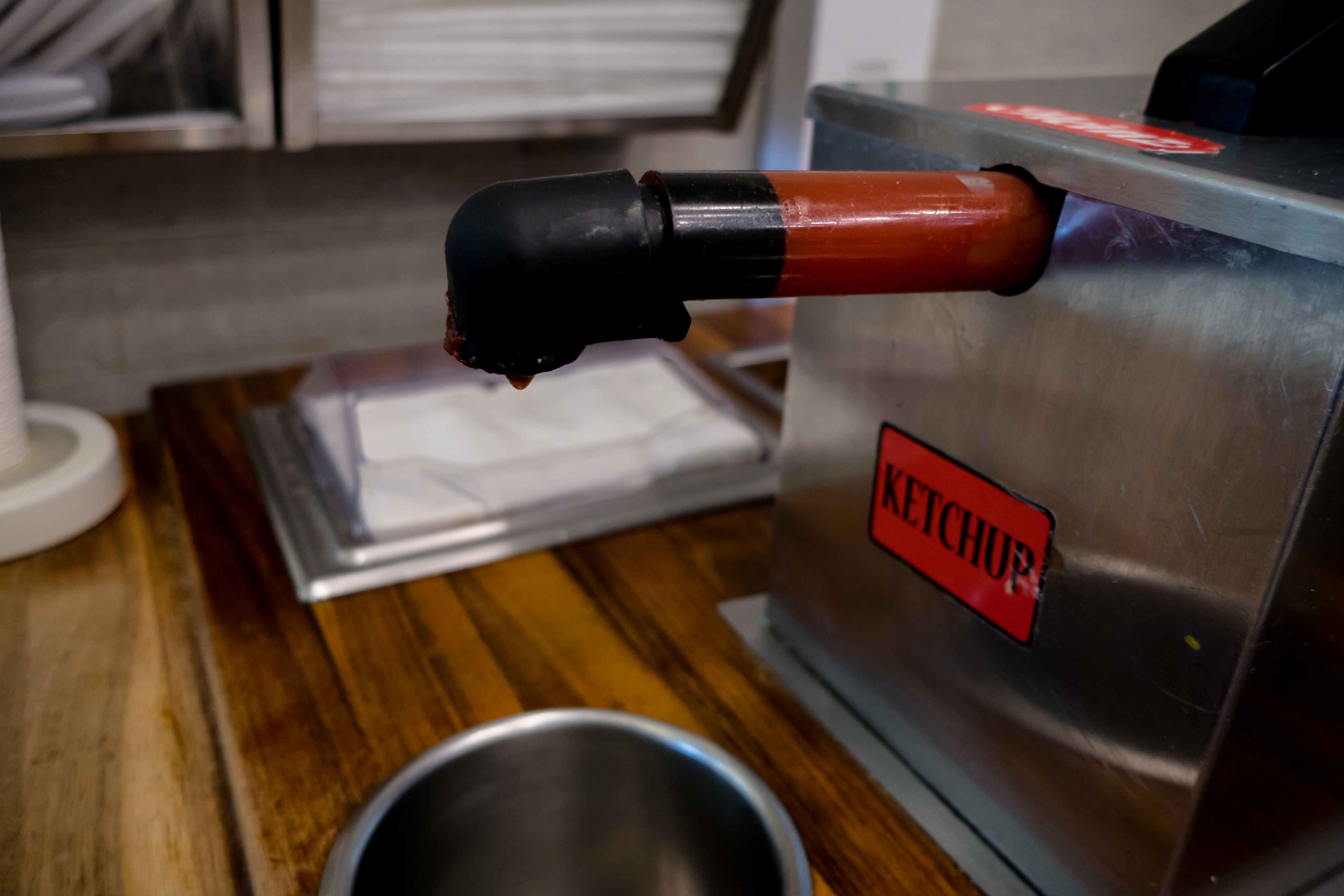 A ketchup pump dispenser with the label &quot;KETCHUP&quot; on it, positioned over a stainless steel container