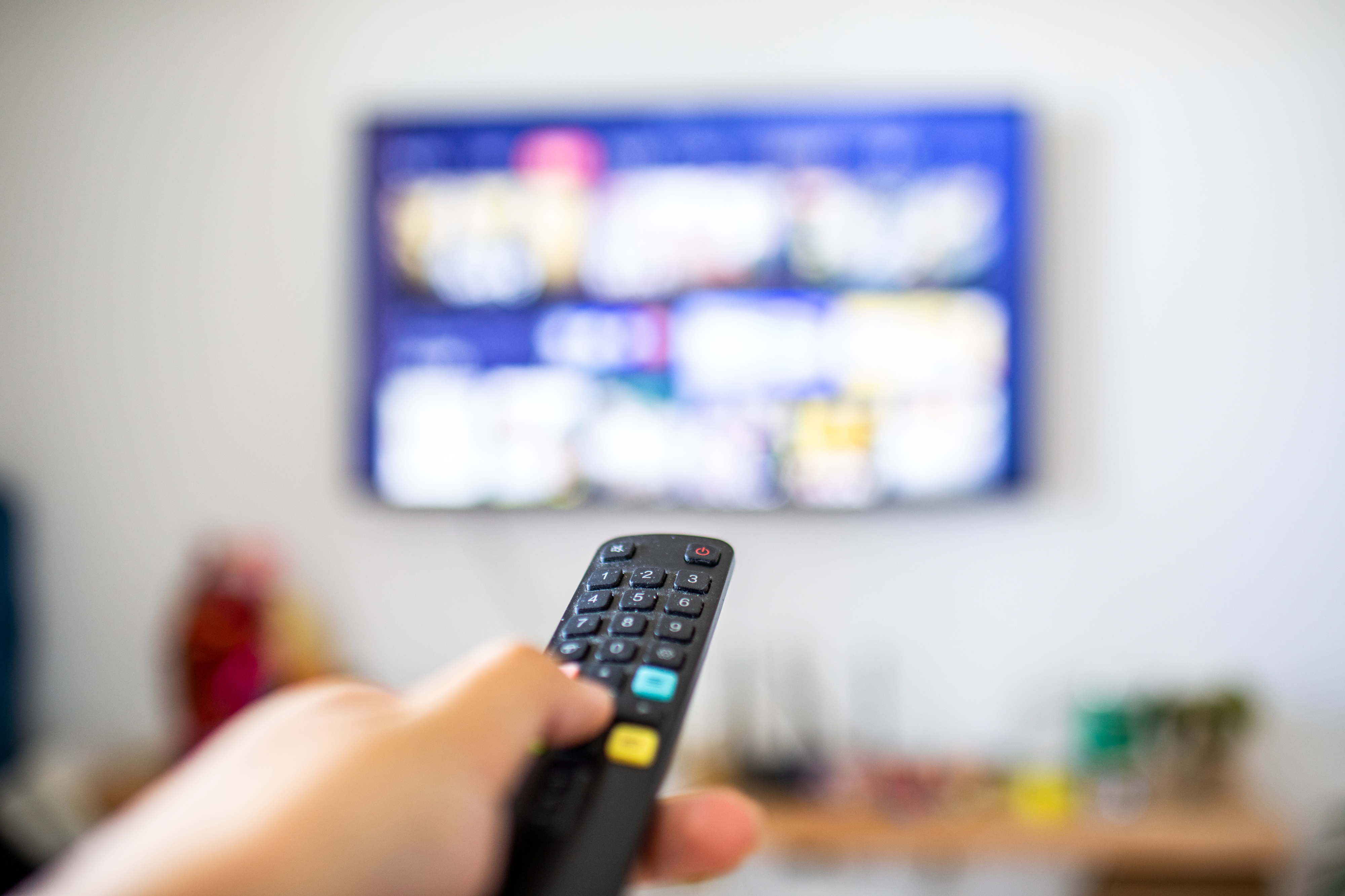 Person holding a remote control with an out-of-focus TV screen in the background