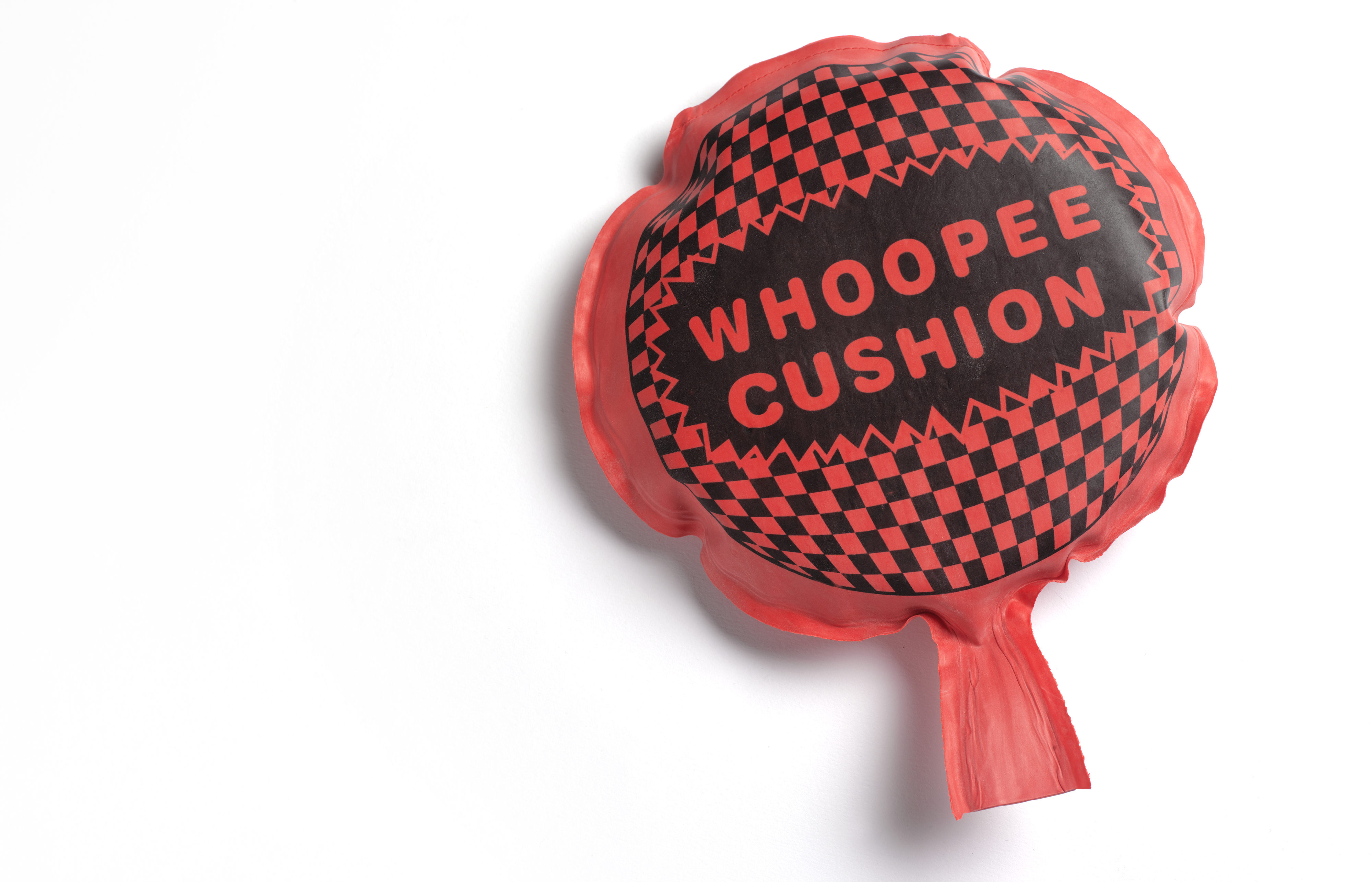 A whoopee cushion with &quot;WHOOPEE CUSHION&quot; text, checkered pattern on top, inflated on white background