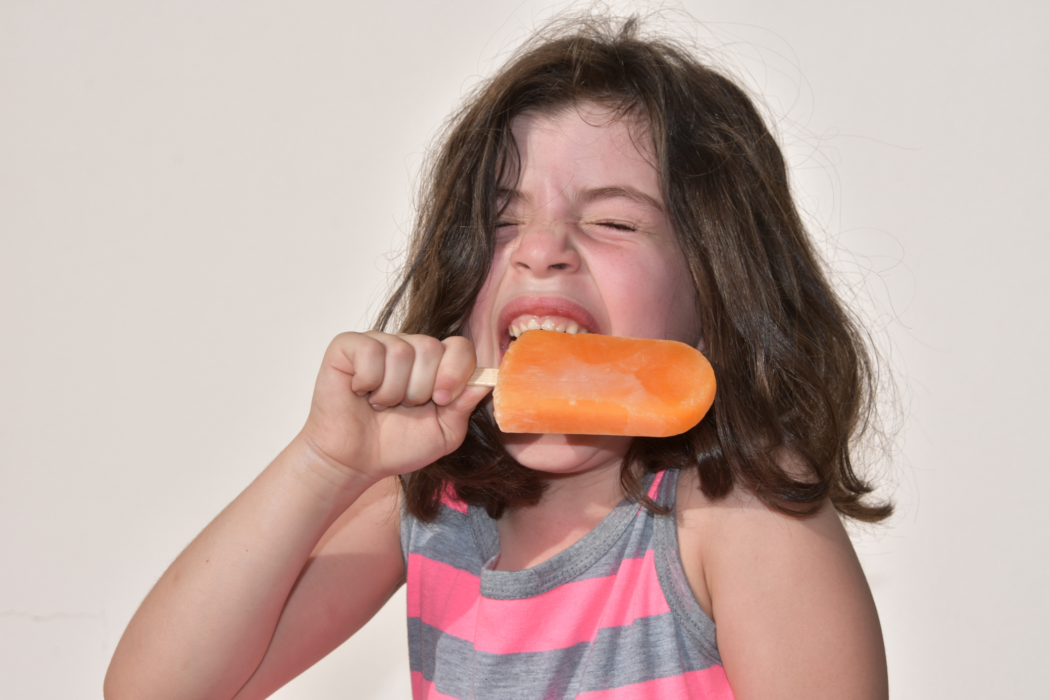 Child bites into a popsicle with a grimace, indicating it may be cold or sour