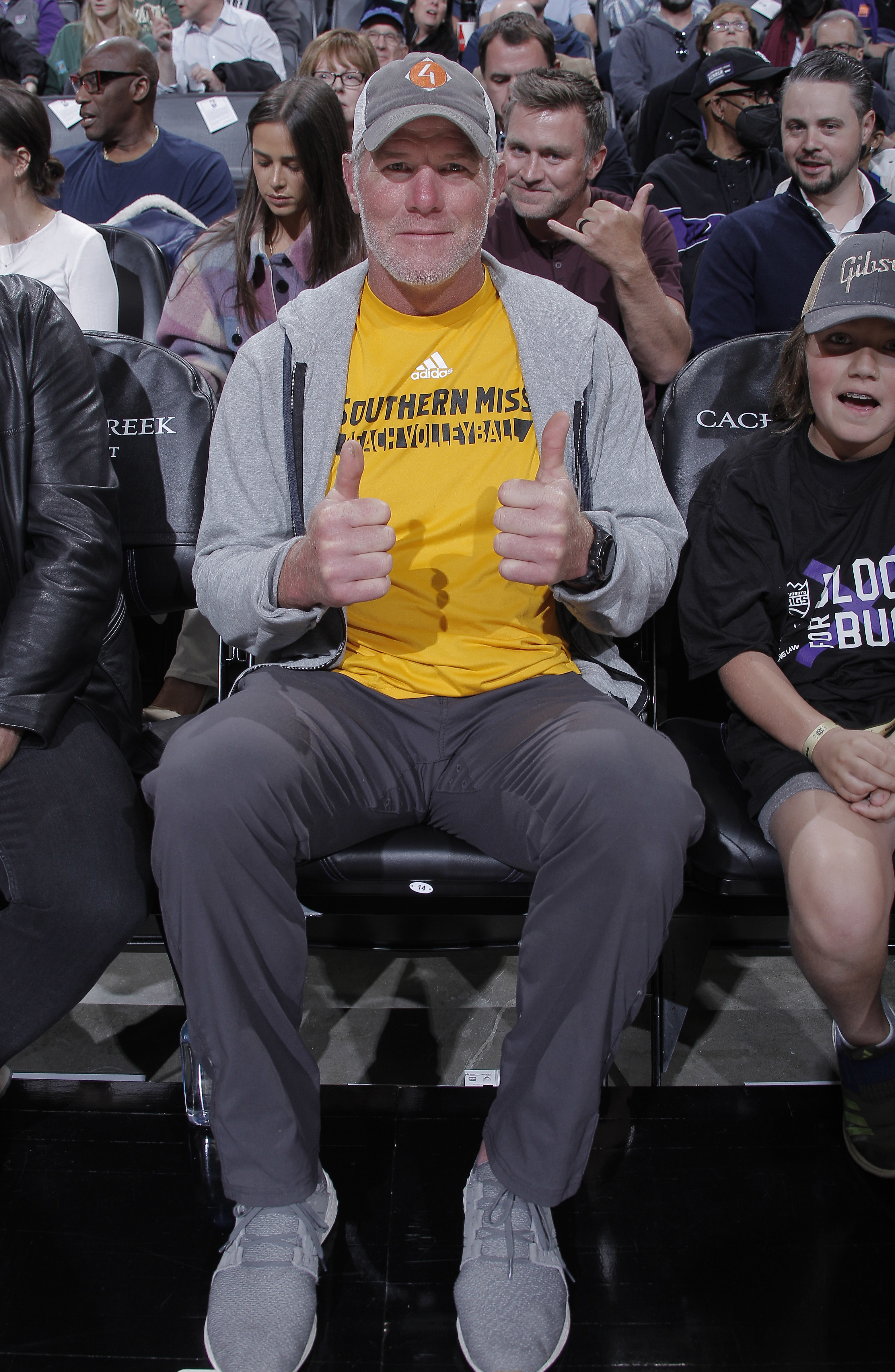 Brett in a Southern Miss T-shirt and cap sitting with thumbs up at an event
