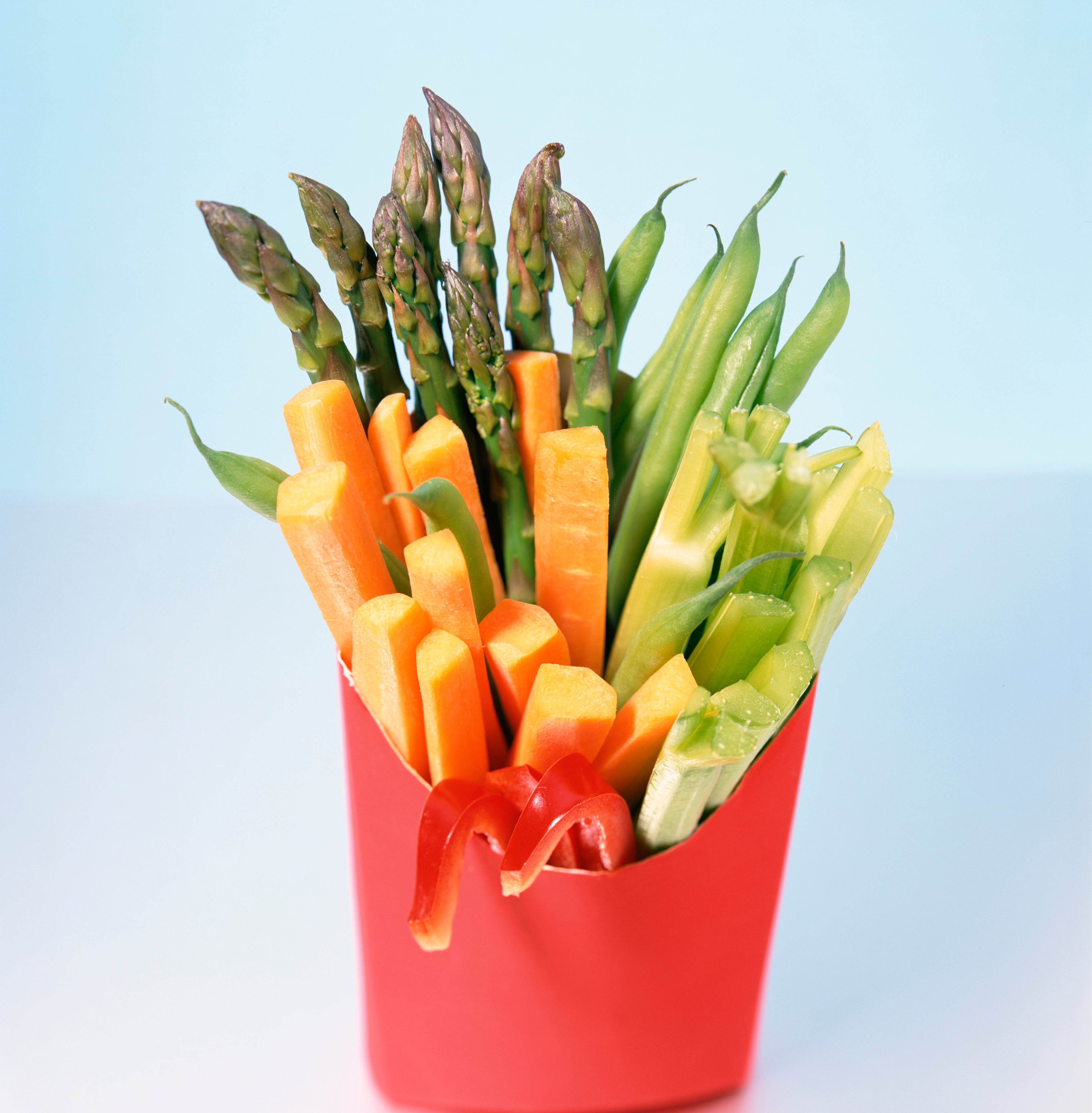 A bouquet of various cut vegetables, including asparagus, presented in a red fast-food container