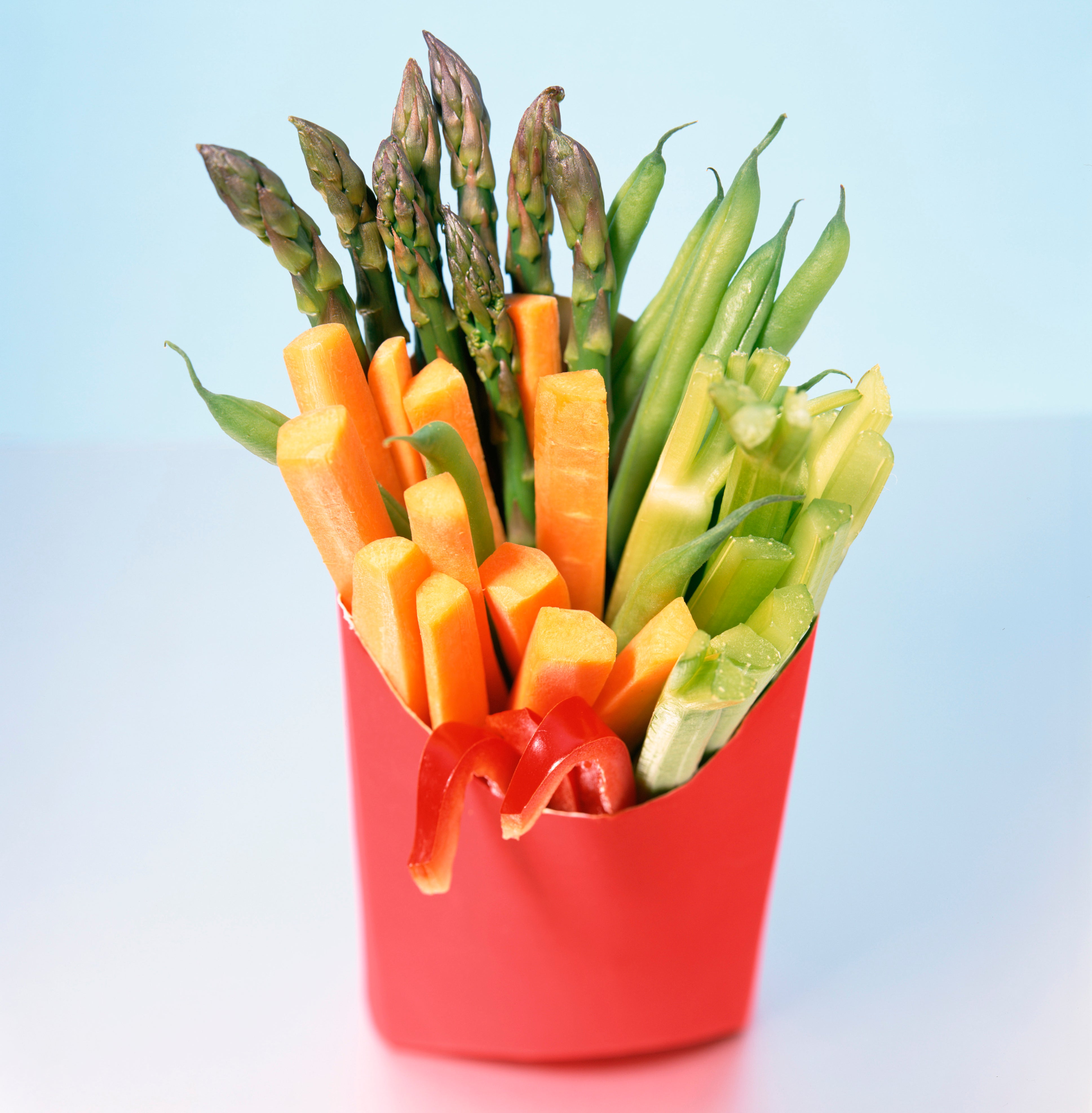 A bouquet of various cut vegetables, including asparagus, presented in a red fast-food container