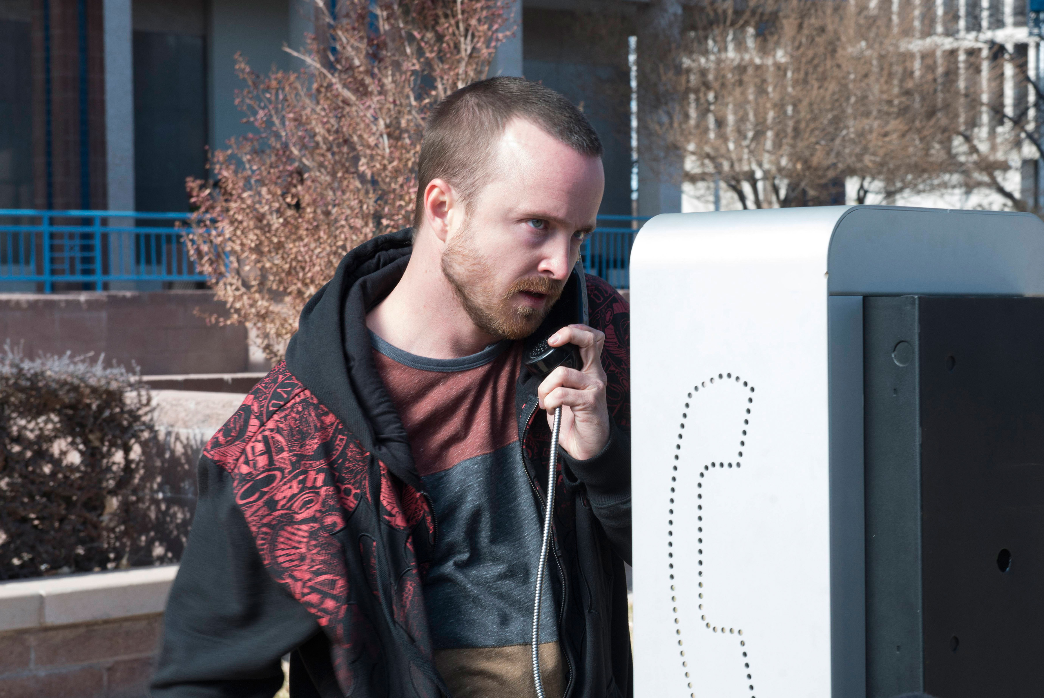 in a scene, Aaron in hoodie using a payphone on a sunny day