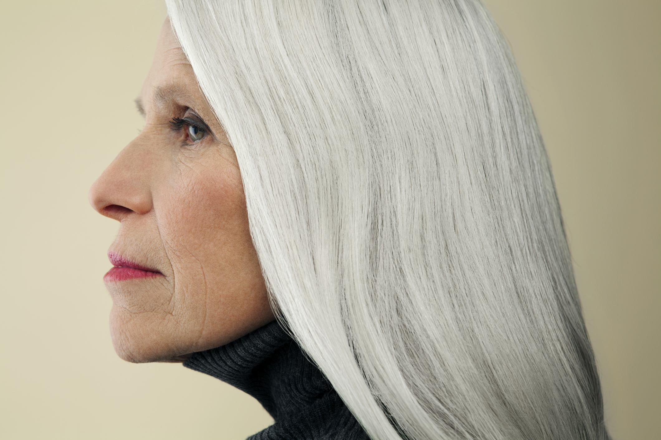 Side profile of an older woman with long, straight gray hair, wearing a turtleneck