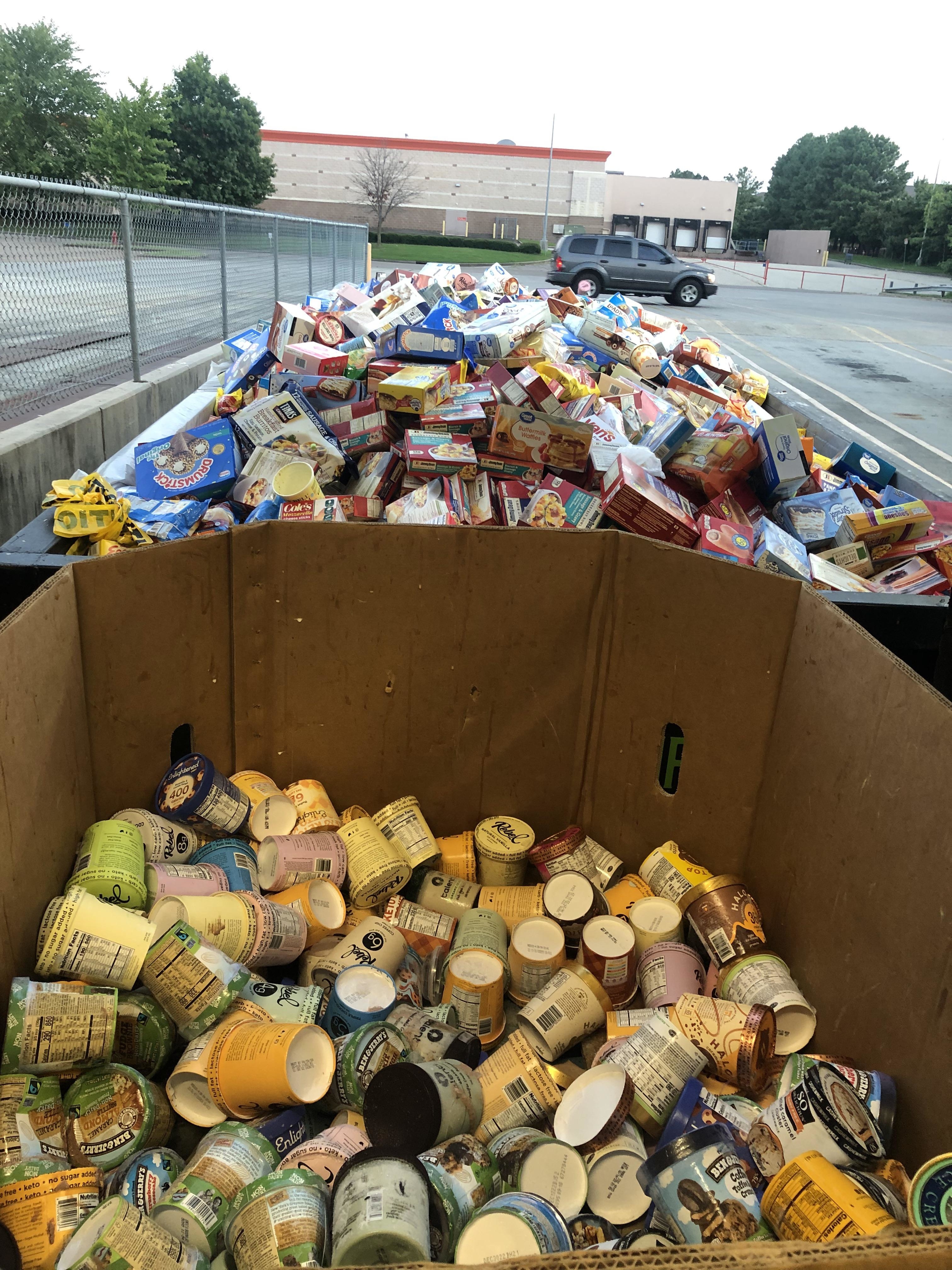 A dumpster overflowing with discarded food items outside a store