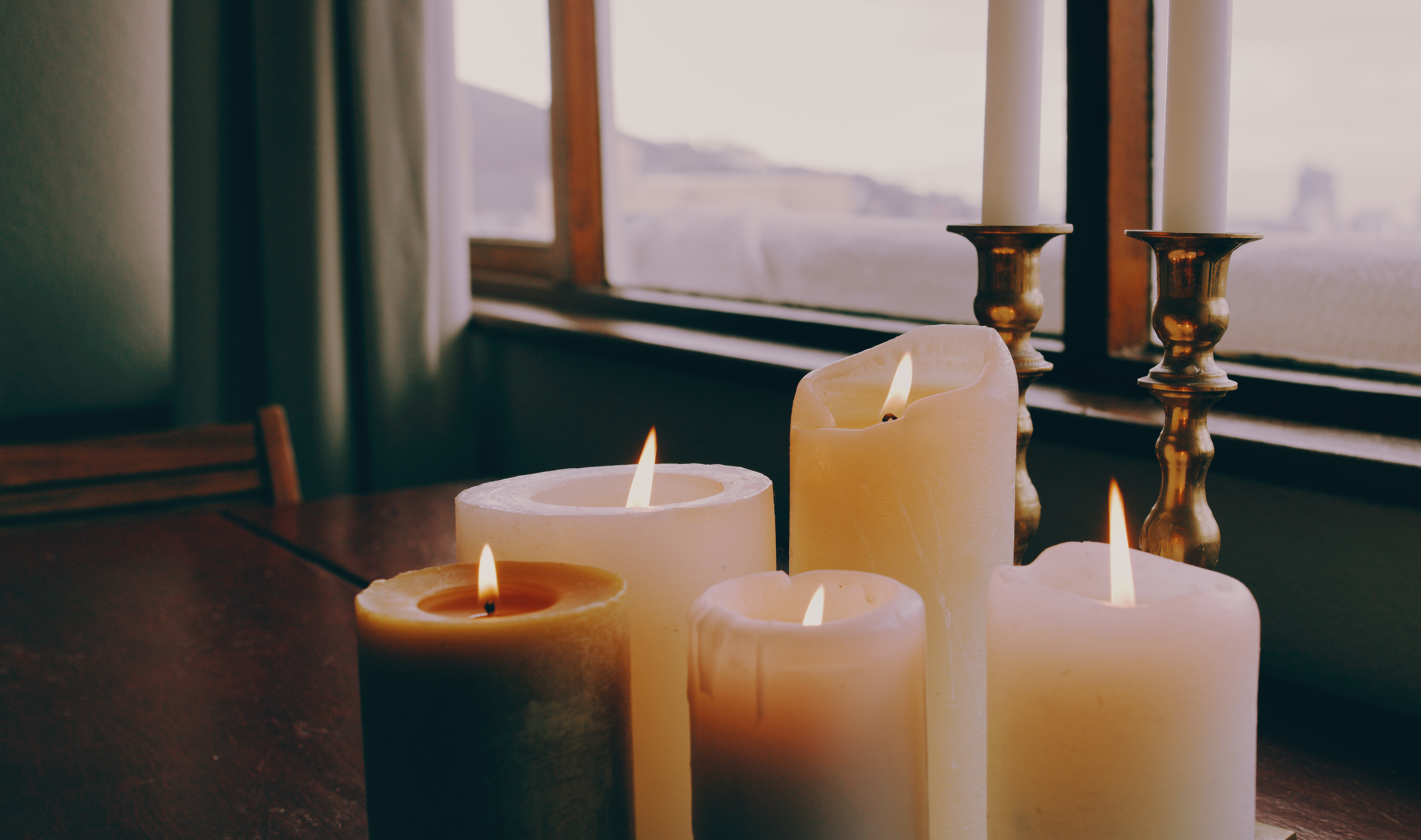 Five lit candles of varying heights on a surface near a window with a view of distant hills