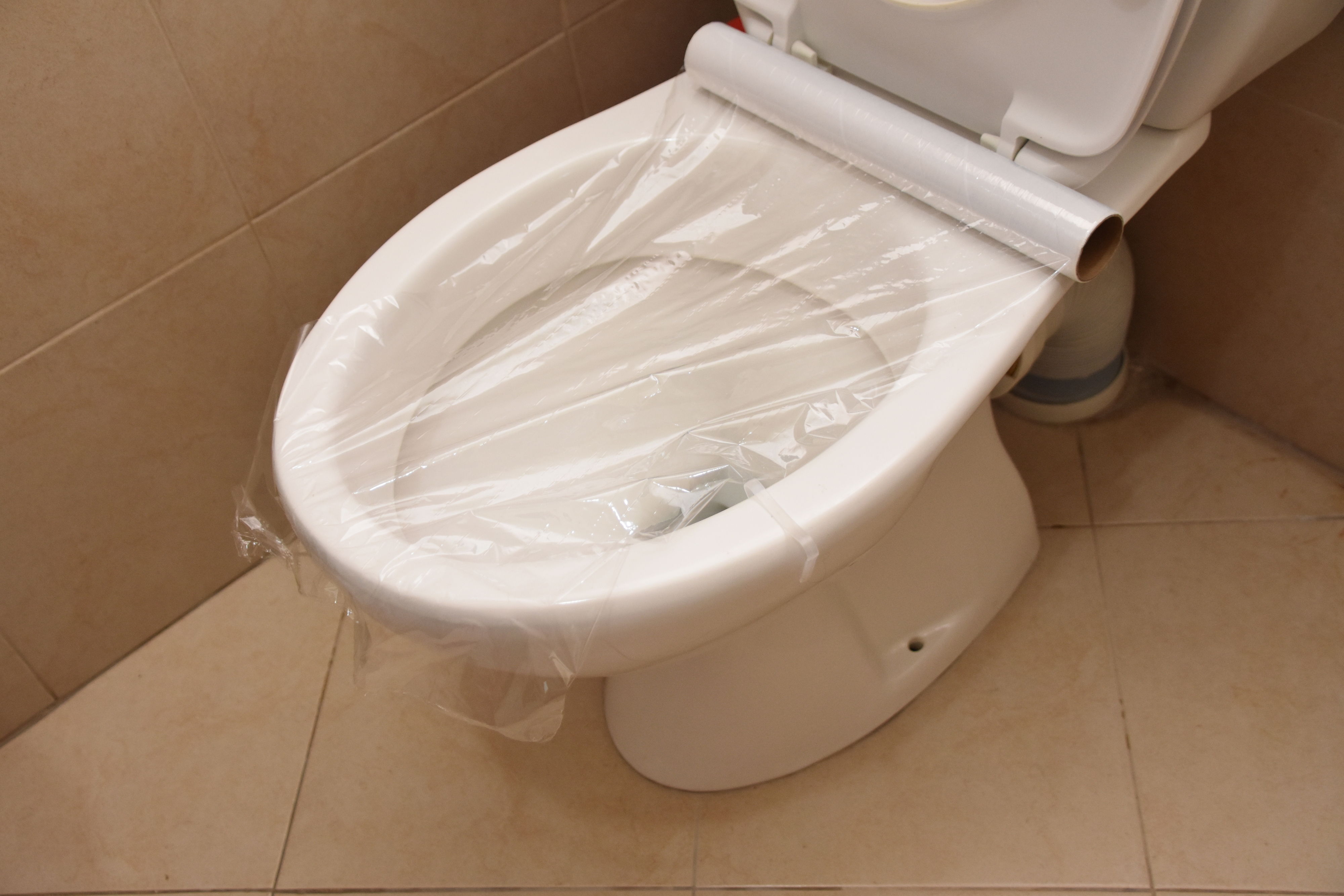 A toilet with plastic wrap covering the top of the bowl