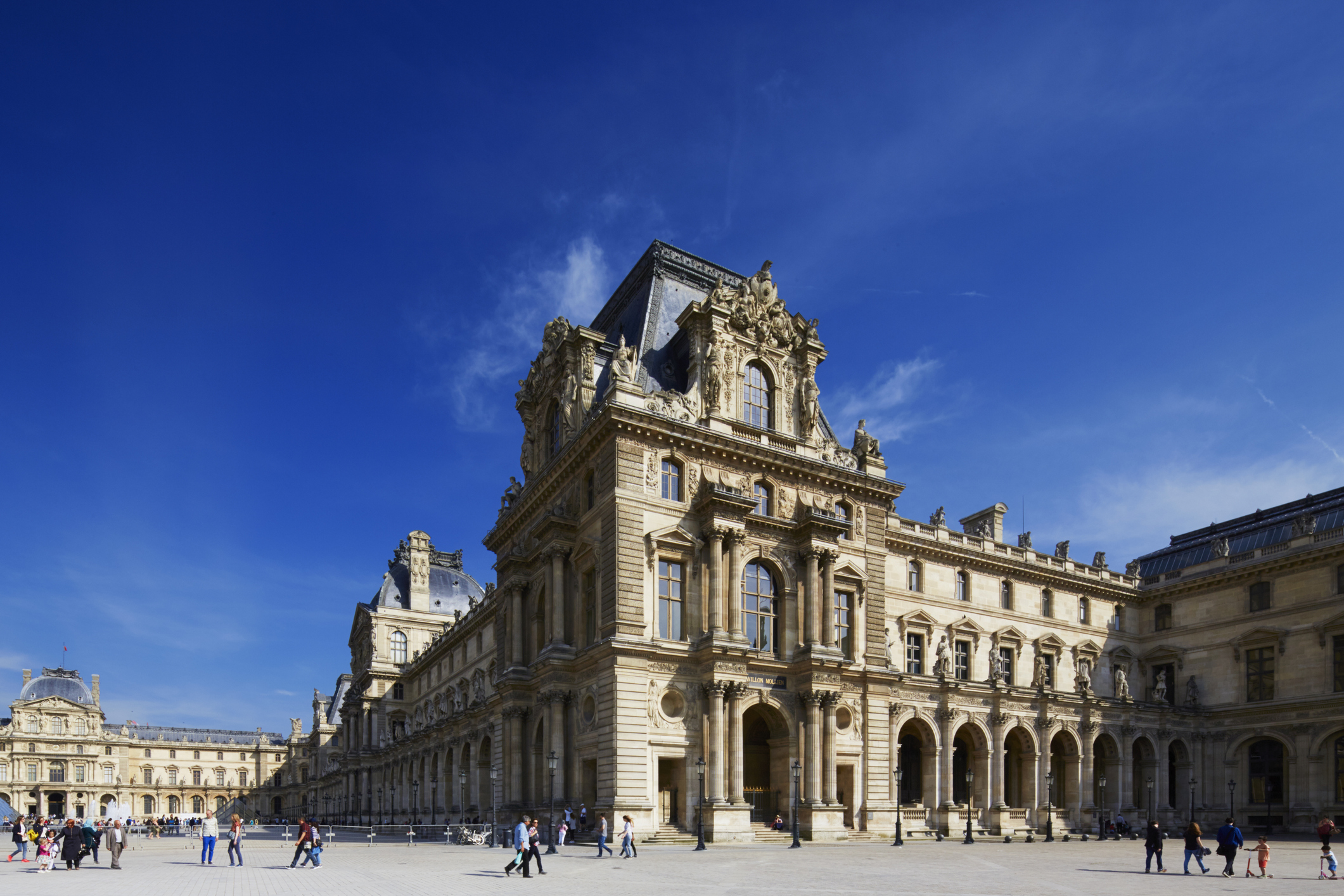 Exterior view of the Louvre Museum in daylight with visitors walking in the courtyard