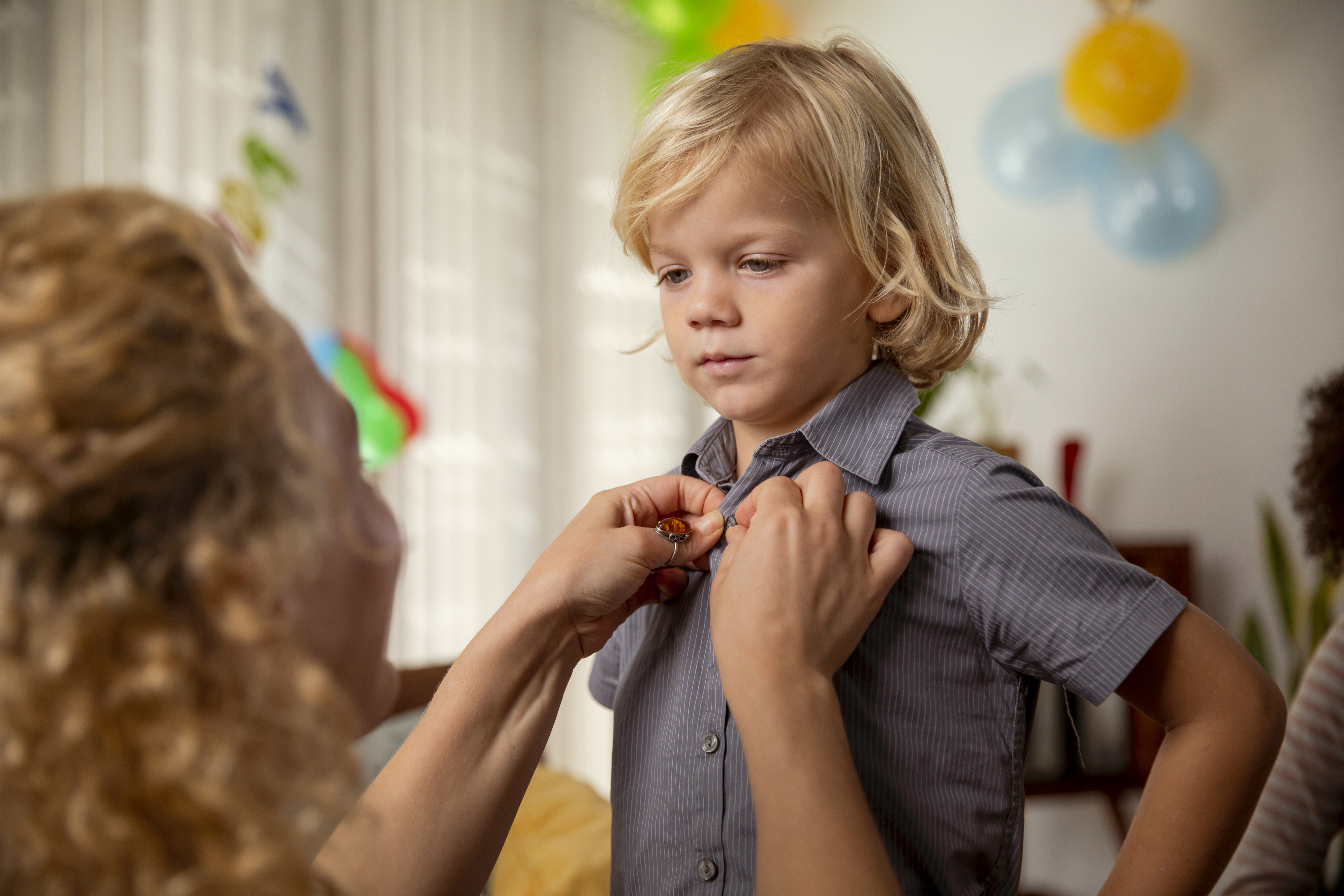 Adult helps a child in a shirt and tie get ready, possibly for a formal event
