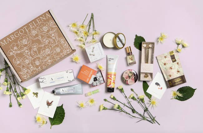 Assorted Margot Elena beauty products and packaging displayed with flowers on a flat surface